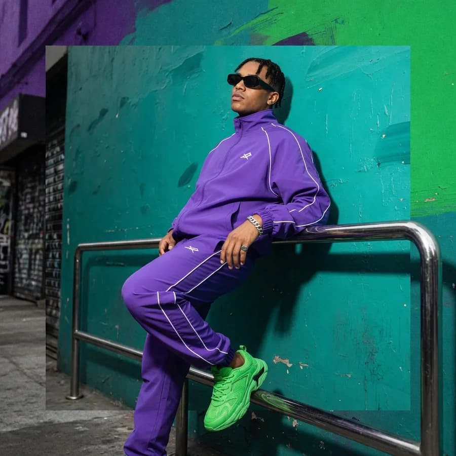 A street style shot generated by Grok Imagine — a violet tracksuit and neon green trainers against a teal wall, hard flash.