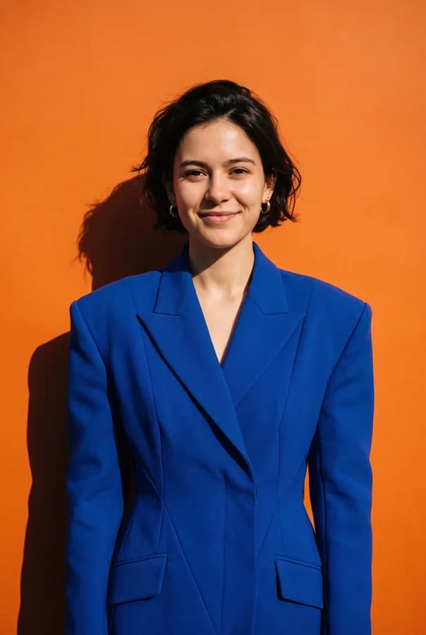 A plain portrait of a woman in a white t-shirt restyled with Nano Banana Pro into a fashion editorial — cobalt blazer, tangerine backdrop, hard sunlight, the same face and pose.